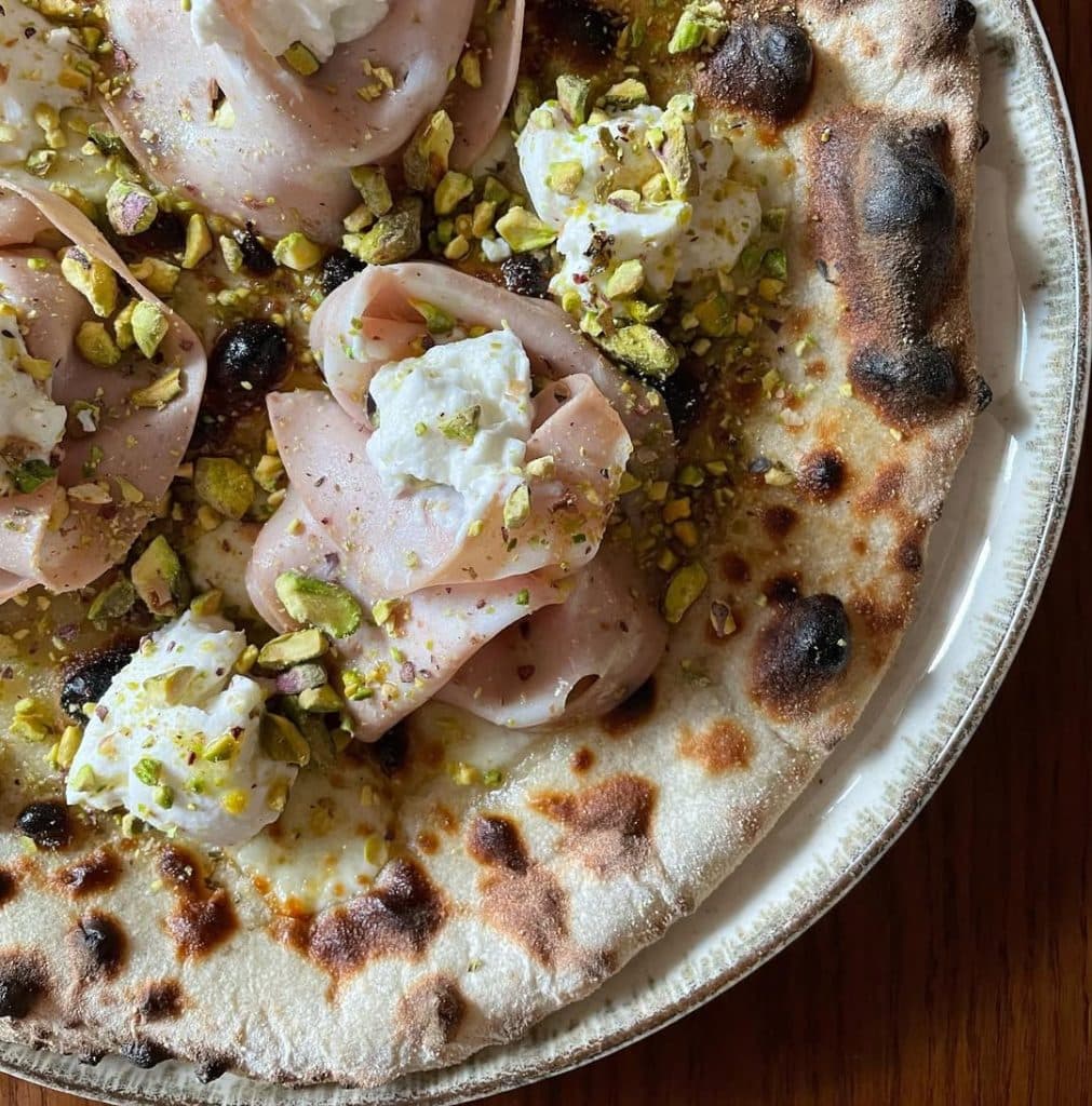 Homemade pizza with mortadella, ricotta, and pistachio. Baked in an Ooni outdoor pizza oven.