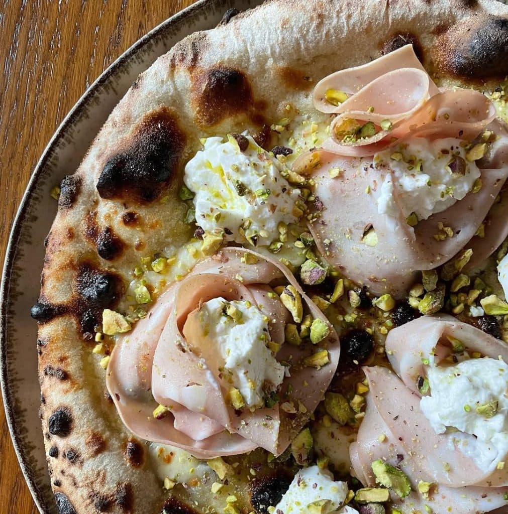 Homemade pizza with mortadella, ricotta, and pistachio. Baked in an Ooni outdoor pizza oven.