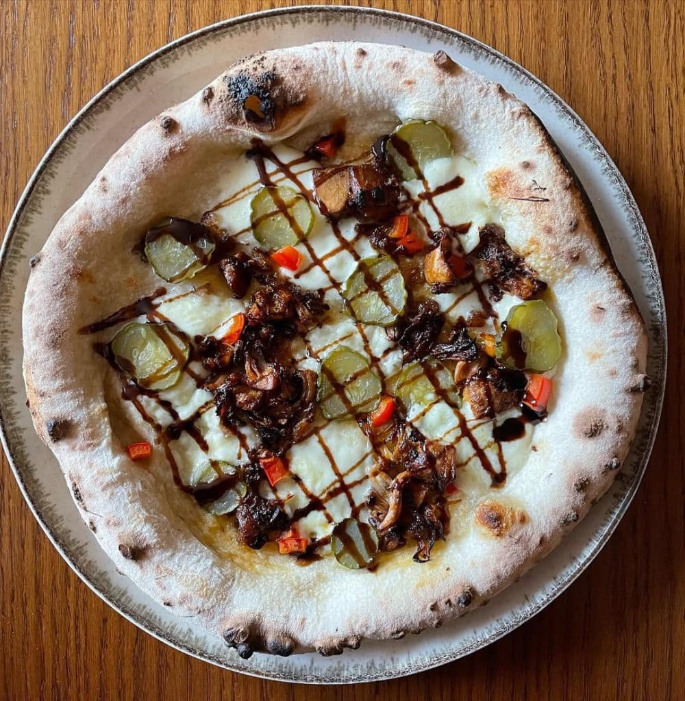Homemade pizza with spiced jackfruit, pickles, red capsicum and balsamic glaze. Baked in an Ooni outdoor pizza oven. 
