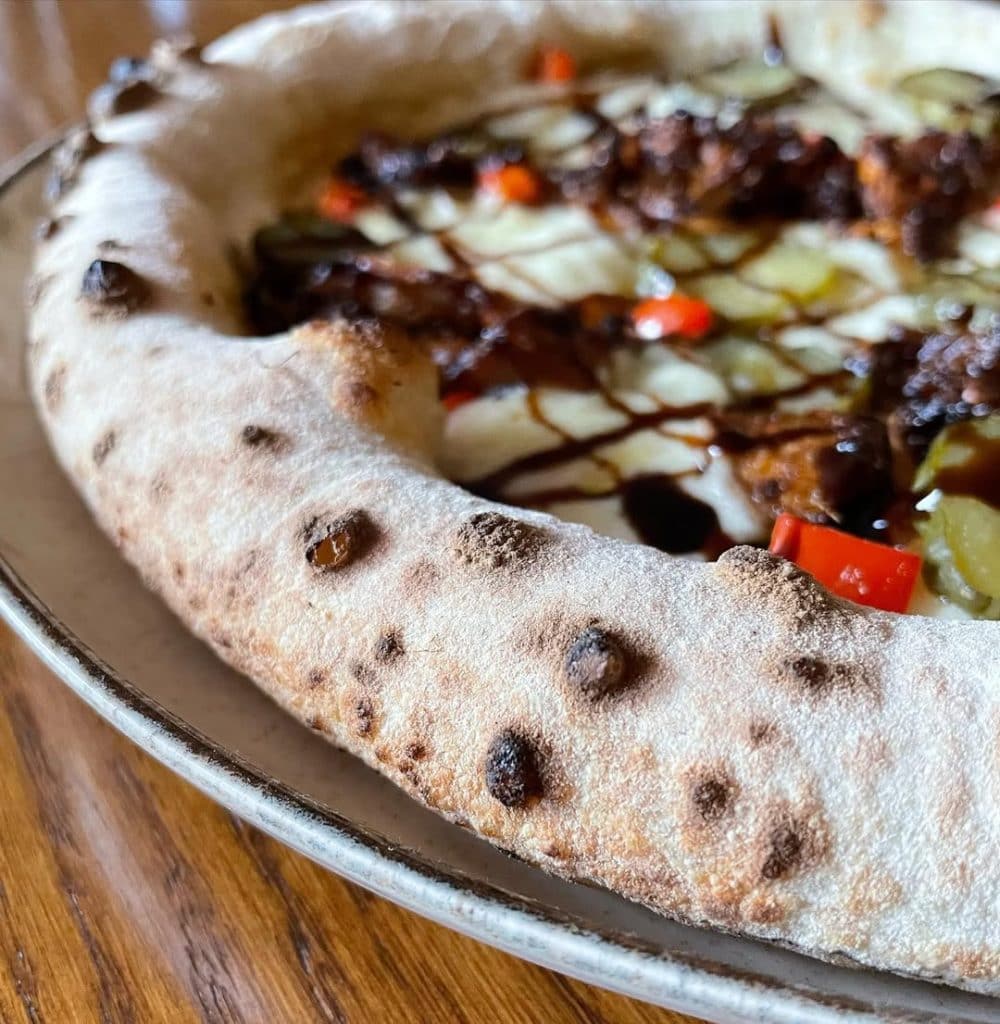 Homemade pizza with spiced jackfruit, pickles, red capsicum and balsamic glaze. Baked in an Ooni outdoor pizza oven.