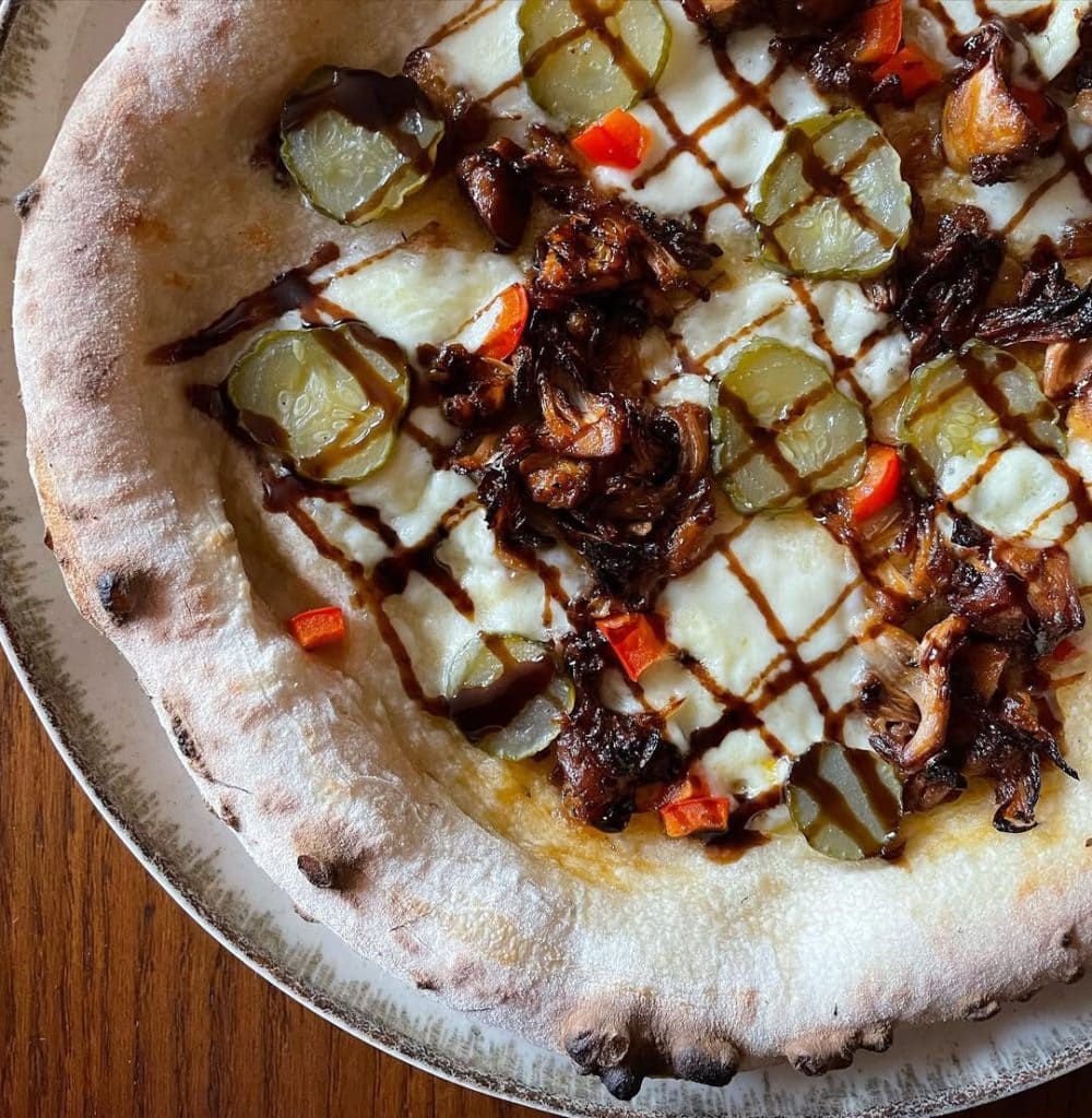 Homemade pizza with spiced jackfruit, pickles, red capsicum and balsamic glaze. Baked in an Ooni outdoor pizza oven.