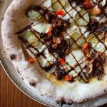 Homemade pizza with spiced jackfruit, pickles, red capsicum and balsamic glaze. Baked in an Ooni outdoor pizza oven.