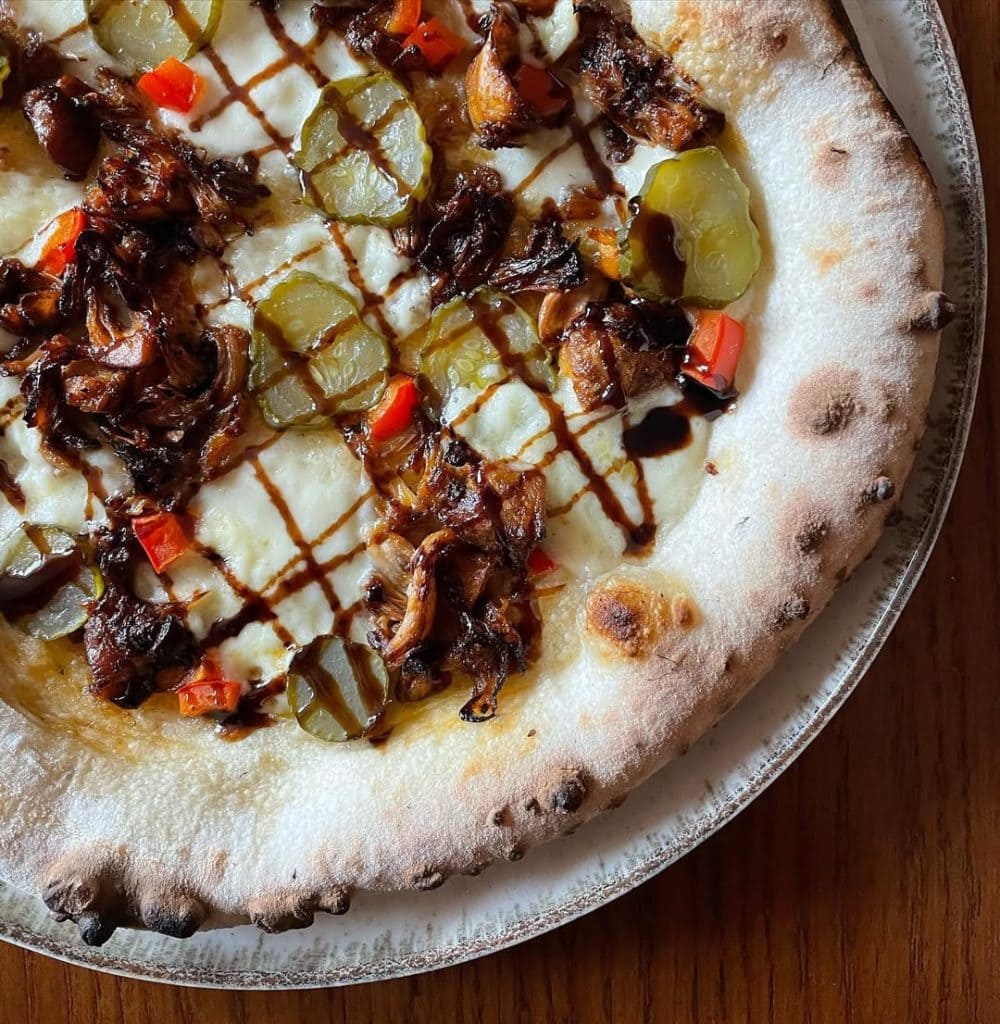 Homemade pizza with spiced jackfruit, pickles, red capsicum and balsamic glaze. Baked in an Ooni outdoor pizza oven.