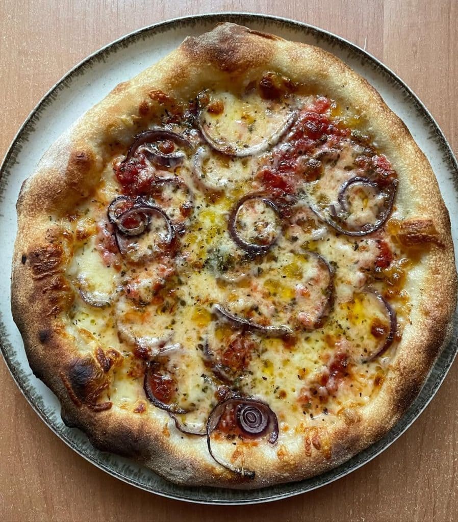 Homemade red onion and mozzarella pizza baked on a pizza steel in a home oven, topped with tomato sauce, melted mozzarella, red onion slices, oregano, and a drizzle of extra virgin olive oil.