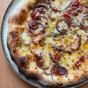 Homemade red onion and mozzarella pizza baked on a pizza steel in a home oven, topped with tomato sauce, melted mozzarella, red onion slices, oregano, and a drizzle of extra virgin olive oil.