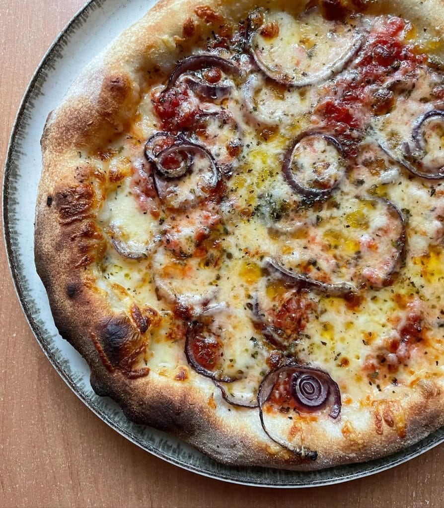 Homemade red onion and mozzarella pizza baked on a pizza steel in a home oven, topped with tomato sauce, melted mozzarella, red onion slices, oregano, and a drizzle of extra virgin olive oil.