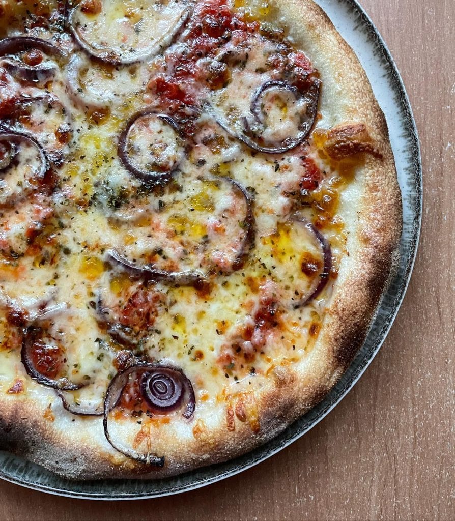 Homemade red onion and mozzarella pizza baked on a pizza steel in a home oven, topped with tomato sauce, melted mozzarella, red onion slices, oregano, and a drizzle of extra virgin olive oil.