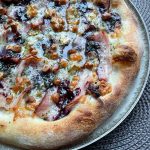 Polish-inspired homemade pizza topped with smoked oscypek cheese, crispy boczek bacon, and cranberry jam on a golden crust, finished with dried parsley and extra virgin olive oil. Baked in a home oven on baking steel.
