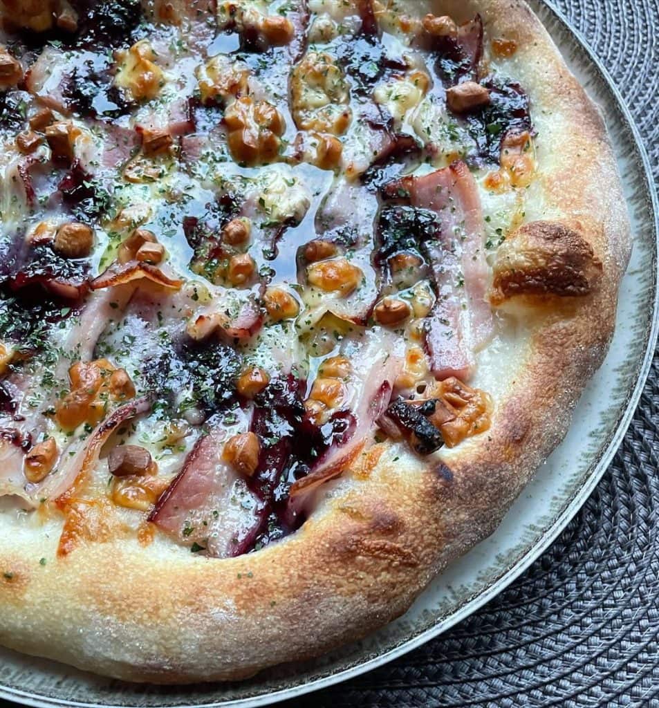 Polish-inspired homemade pizza topped with smoked oscypek cheese, crispy boczek bacon, and cranberry jam on a golden crust, finished with dried parsley and extra virgin olive oil. Baked in a home oven on baking steel.