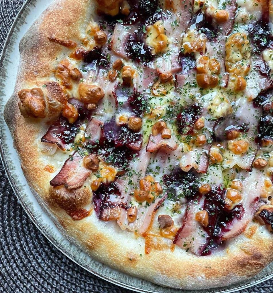 Polish-inspired homemade pizza topped with smoked oscypek cheese, crispy boczek bacon, and cranberry jam on a golden crust, finished with dried parsley and extra virgin olive oil. Baked in a home oven on baking steel.