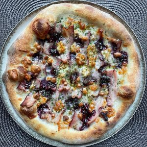 Polish-inspired homemade pizza topped with smoked oscypek cheese, crispy boczek bacon, and cranberry jam on a golden crust, finished with dried parsley and extra virgin olive oil. Baked in a home oven on baking steel.