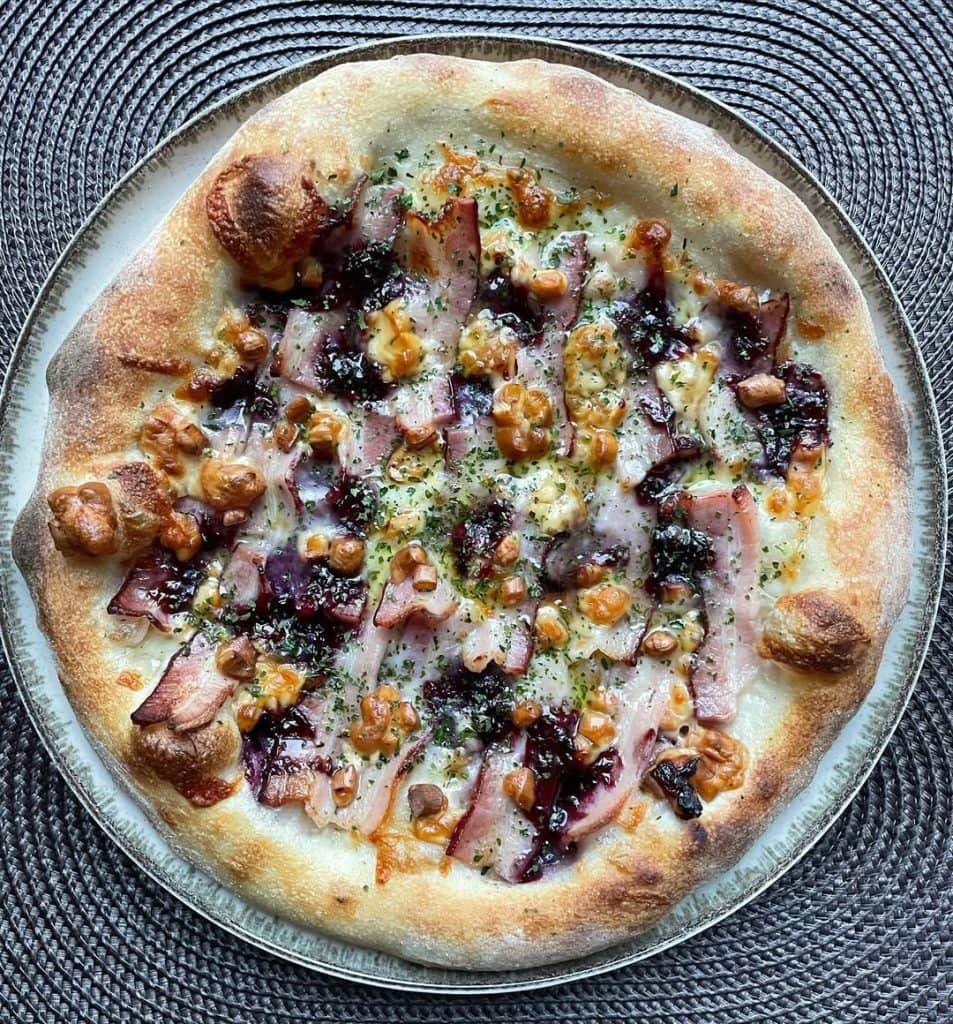 Polish-inspired homemade pizza topped with smoked oscypek cheese, crispy boczek bacon, and cranberry jam on a golden crust, finished with dried parsley and extra virgin olive oil. Baked in a home oven on baking steel.