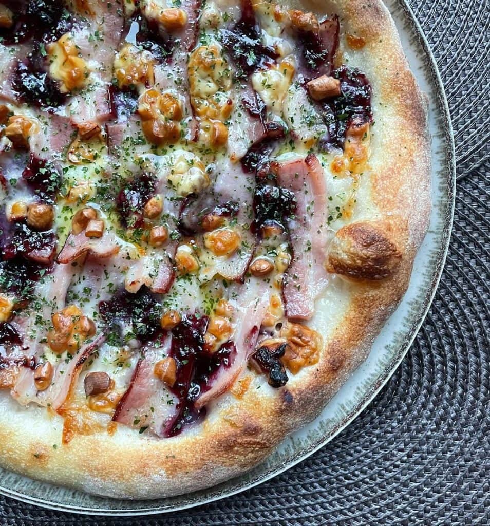 Polish-inspired homemade pizza topped with smoked oscypek cheese, crispy boczek bacon, and cranberry jam on a golden crust, finished with dried parsley and extra virgin olive oil. Baked in a home oven on baking steel.