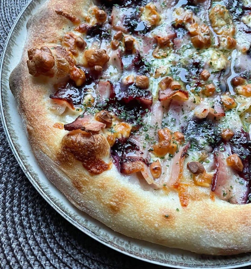 Polish-inspired homemade pizza topped with smoked oscypek cheese, crispy boczek bacon, and cranberry jam on a golden crust, finished with dried parsley and extra virgin olive oil. Baked in a home oven on baking steel.
