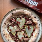 Pizza with Nutella, pear slices, crushed Tim Tam biscuits, chopped peanuts, and bright pomegranate arils on a golden crust, served warm on a wooden board.