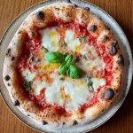 Neapolitan-style Margherita pizza topped with tomato sauce, melted mozzarella, basil leaves added before and after baking, and a drizzle of olive oil, showcasing a puffy, golden crust from a long room-temperature fermentation