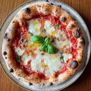 Neapolitan-style Margherita pizza topped with tomato sauce, melted mozzarella, basil leaves added before and after baking, and a drizzle of olive oil, showcasing a puffy, golden crust from a long room-temperature fermentation